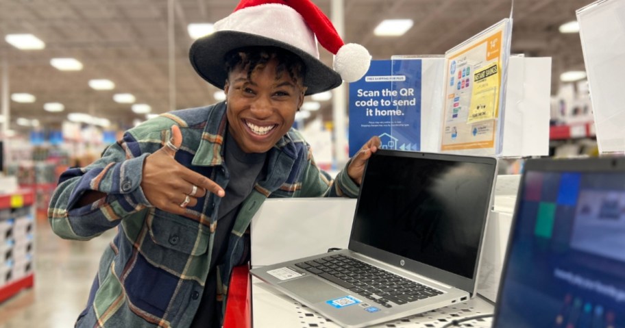 woman wearing a Santa hat pointing at a laptop that's on display at Sam's Club