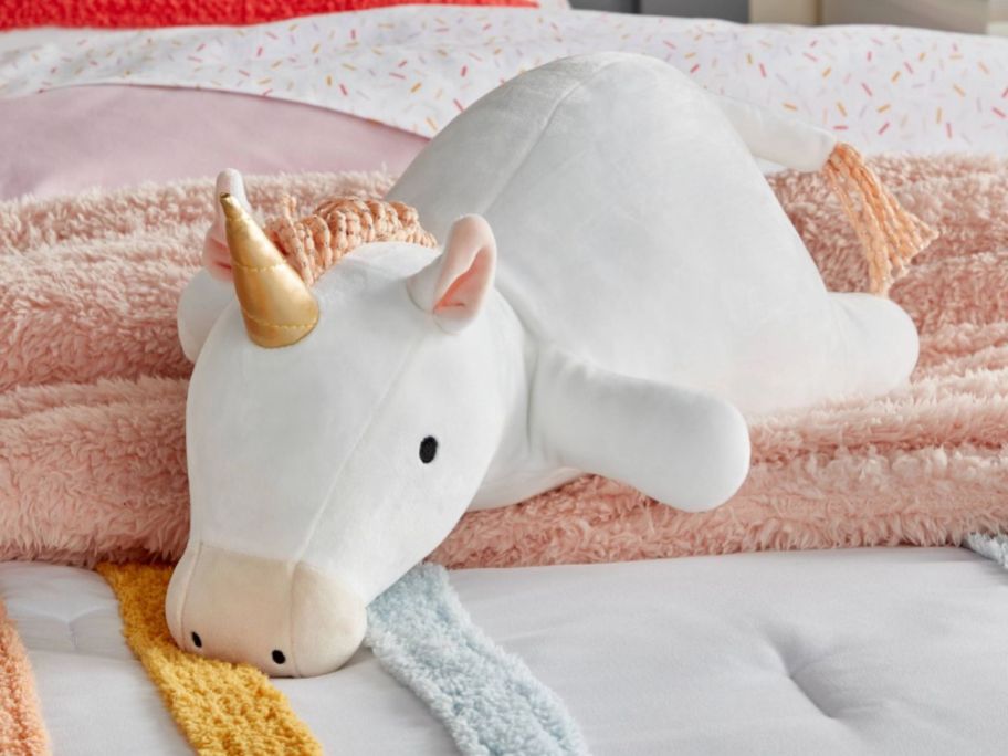 a pillowfort weighted unicorn plush on a bed.