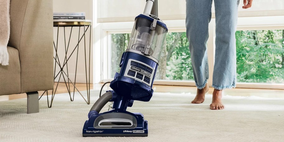 person pushing blue and gray shark vacuum on carpet 