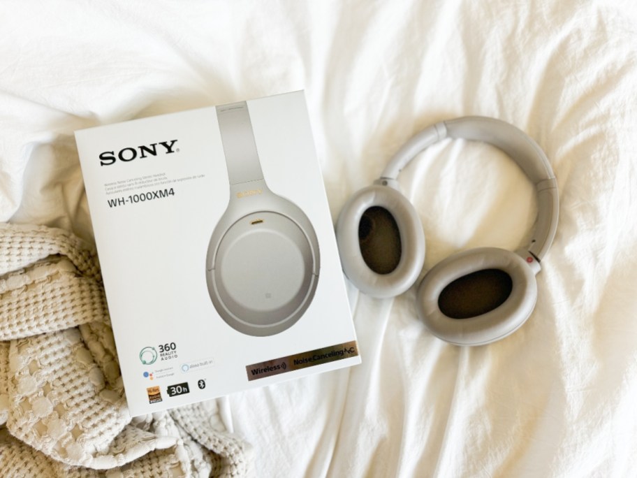 pair of silver Sony headphones on a bed next to the box they come in