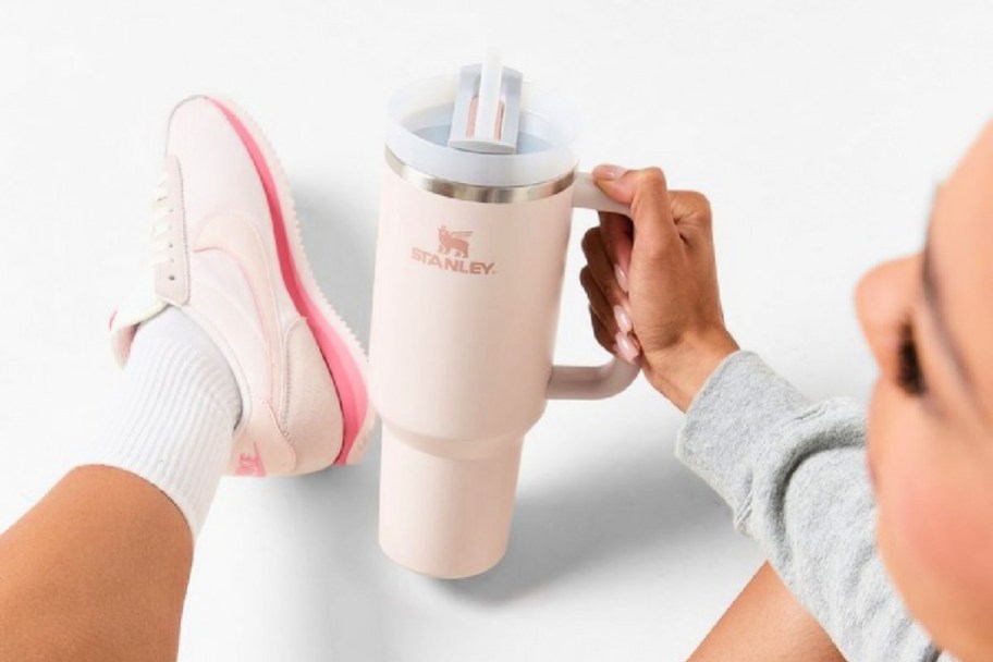 woman sitting on the floor while holding a pink stanley tumbler