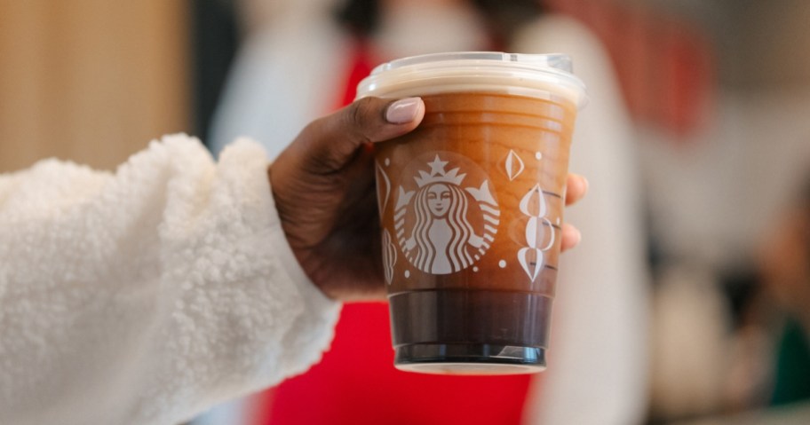 hand holding a clear Starbucks cup with coffee in it, the design on the cup is Christmas / winter holiday themed