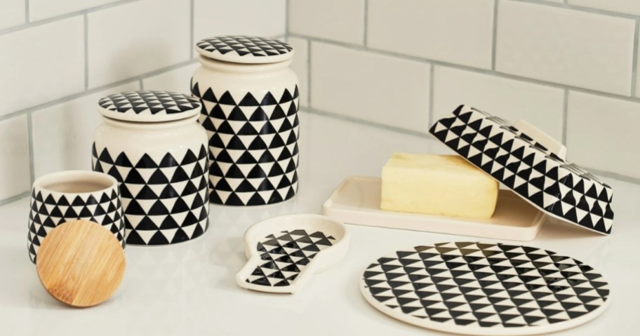 a black and white canister set, spoon rest, butter dish with lid and trivet on a kitchen counter