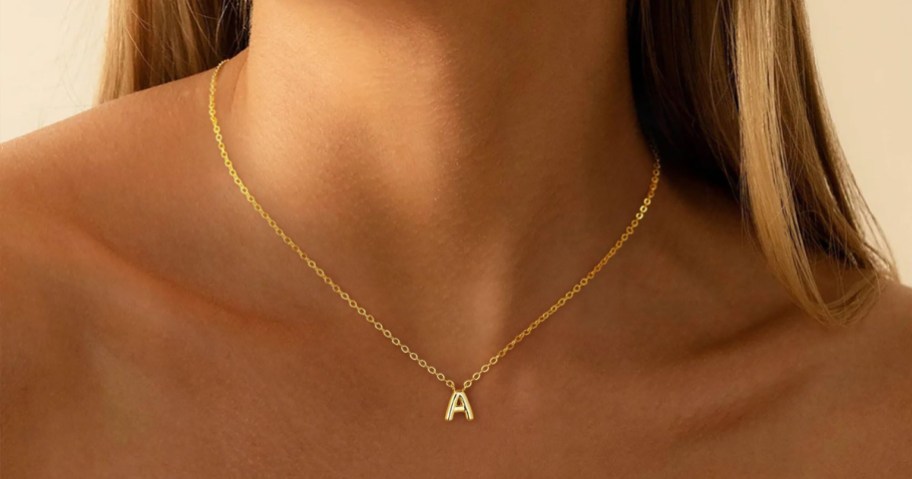 woman's bare neck with a gold bubble letter necklace around it