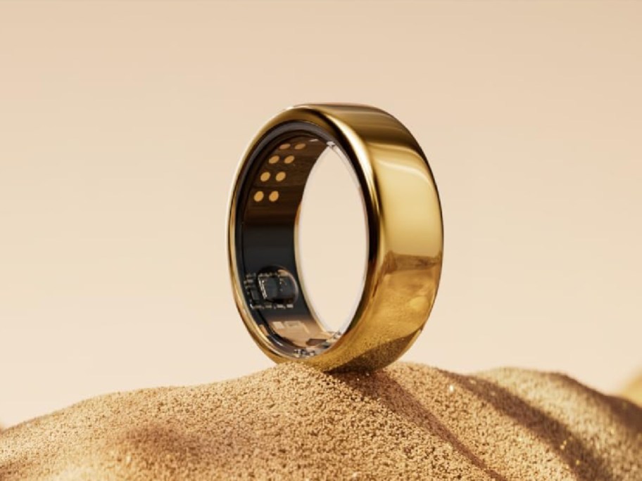 Oura ring in gold displayed on the sand