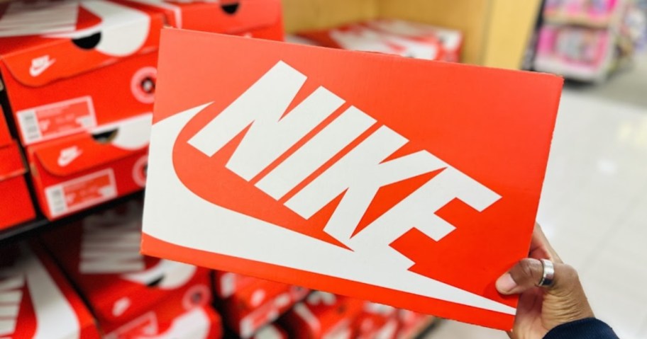 a womans hand grabbing an orange nike box off a store shelf