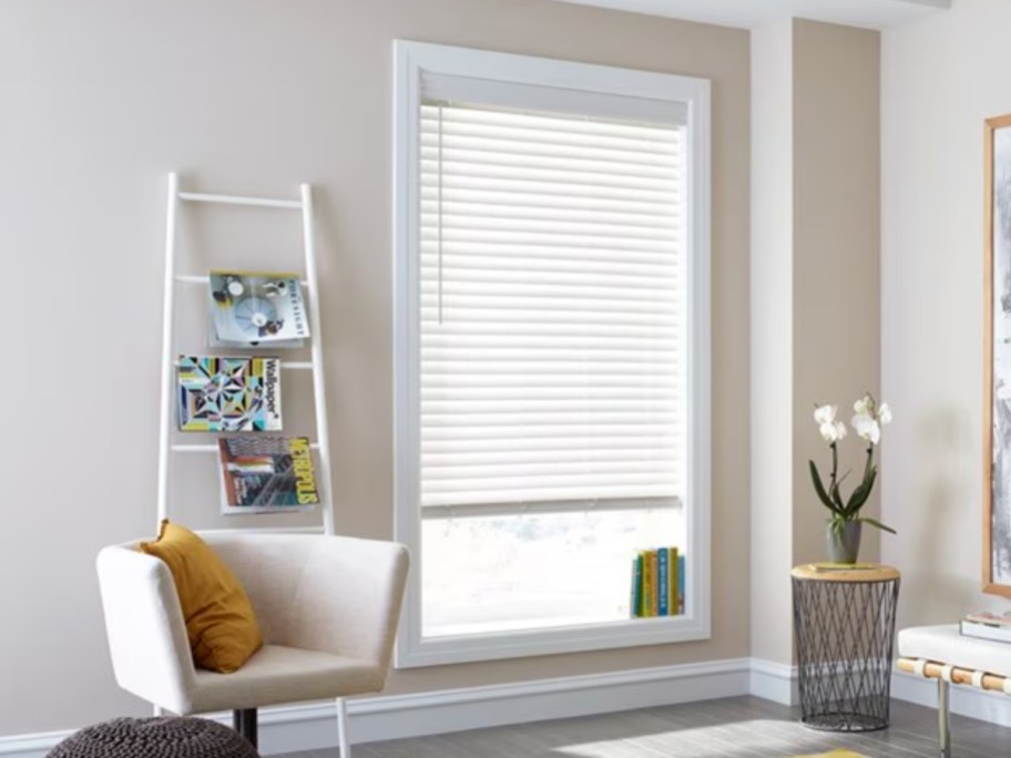 part of a living room with a chair and ladder bookcase and a window with a blind partially up