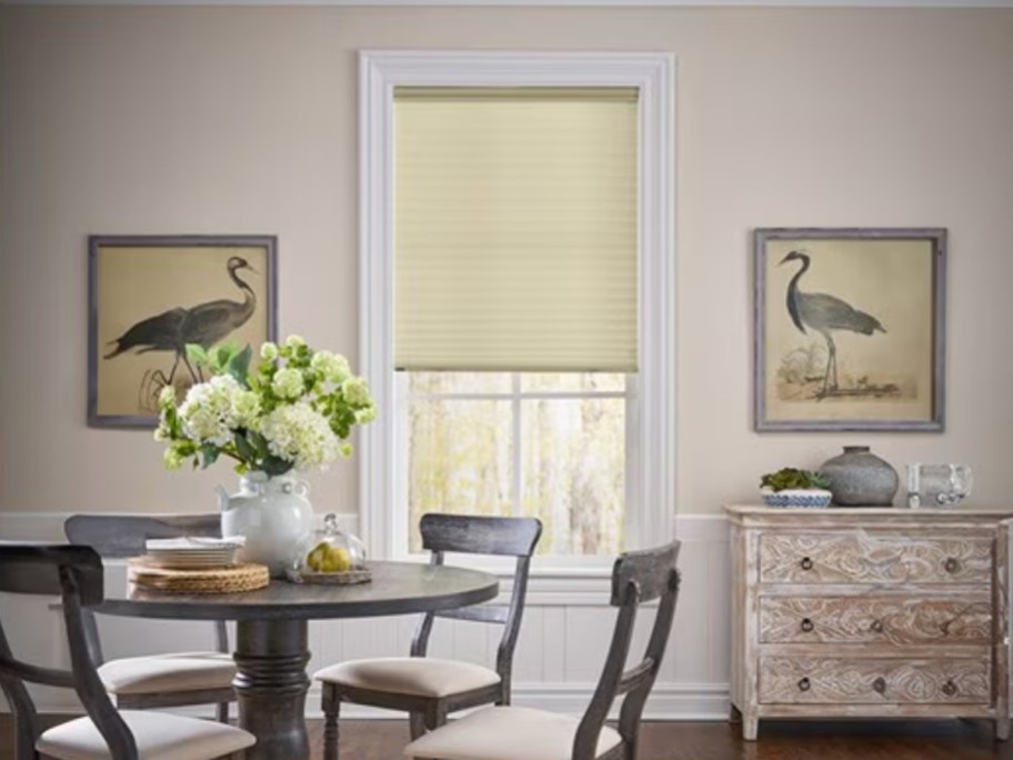 a dining room with a table and chairs and wall decor showing a window with a custom cream color window shade