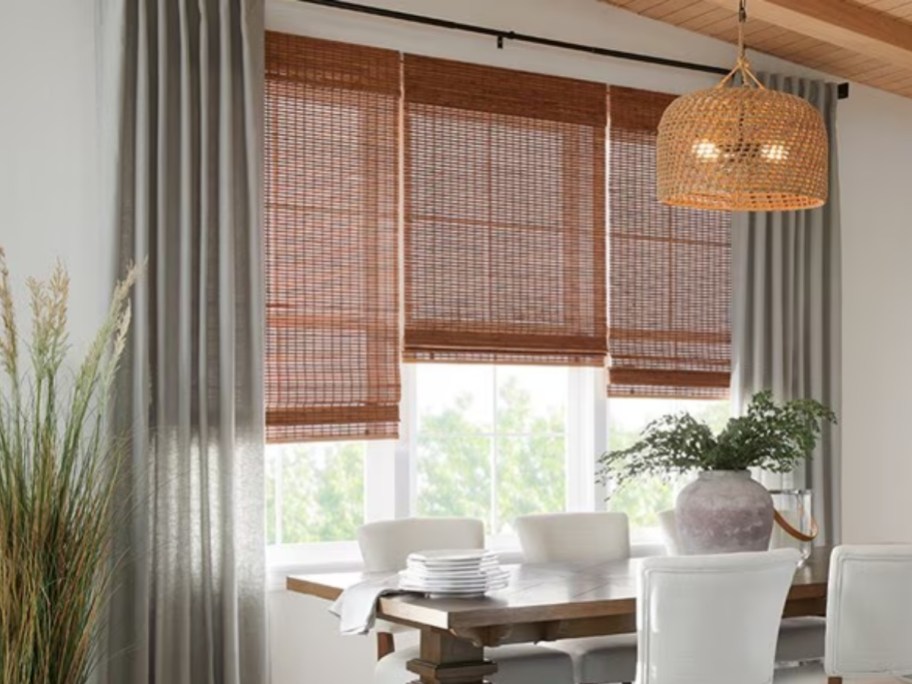 a dining room with table and white upholstered chairs facing a window with reddish brown woven shades partially up