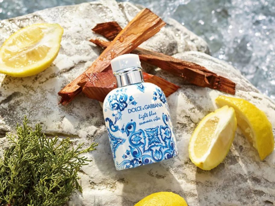 A bottle of Dolce&Gabbana Light blue for men on a rock surrounded by lemons and driftwood