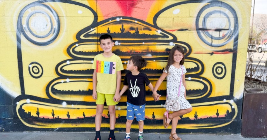 3 kids standing in front of a painted mural on a wall