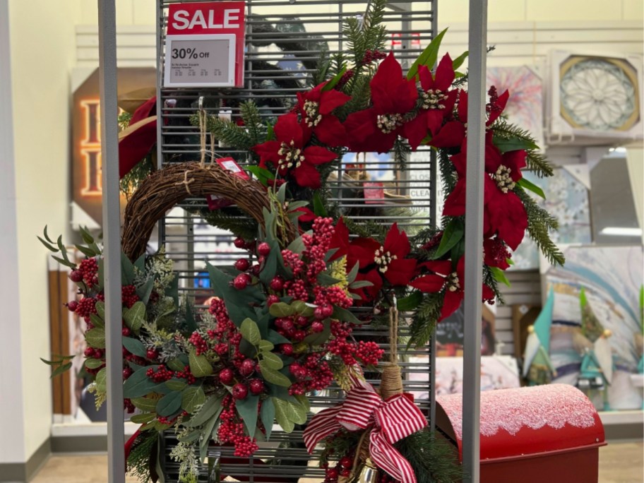 Christmas wreaths with red poinsettias hanging on a display in a Kohl's store