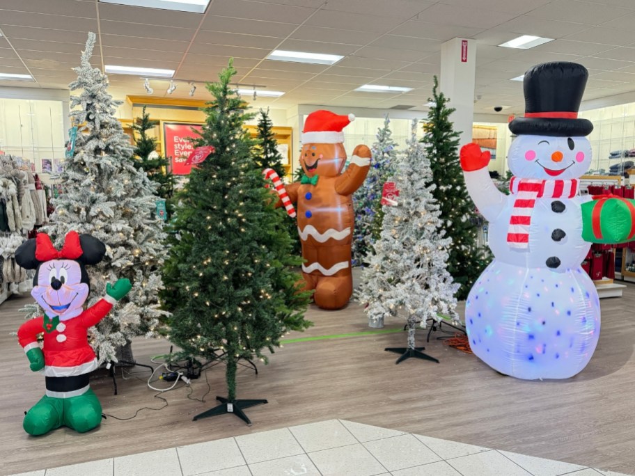 the Christmas section in a Kohl's store with Christmas trees, some green, some white flocked, and large Christmas Inflatable Snowman, Gingerbread man, and Minnie Mouse