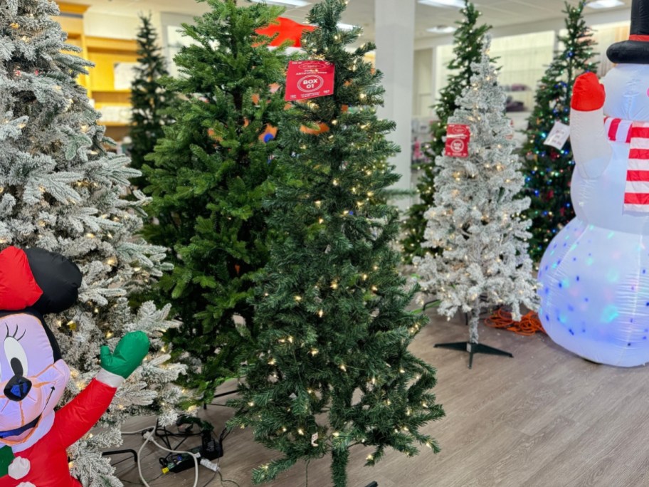 artificial Christmas trees in different sizes and colors in a Kohl's store, you can see part of a large Snowman inflatable 