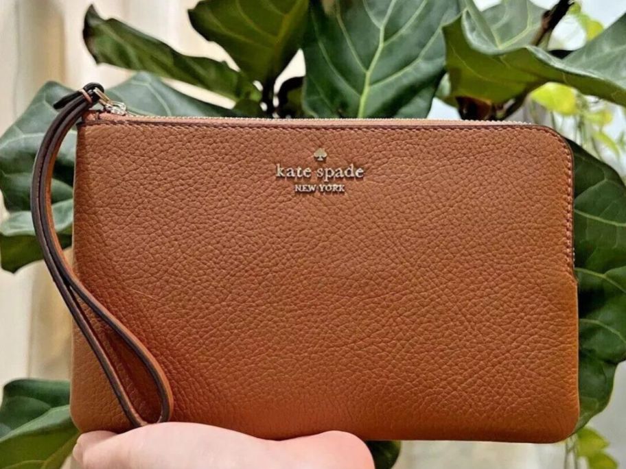 A hand holding a Kate Spade Wristlet in brown