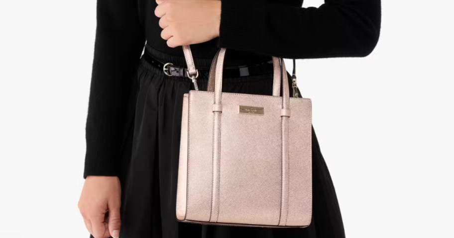 a woman wearing a black dress with a light pink rose gold cross body bag with handles