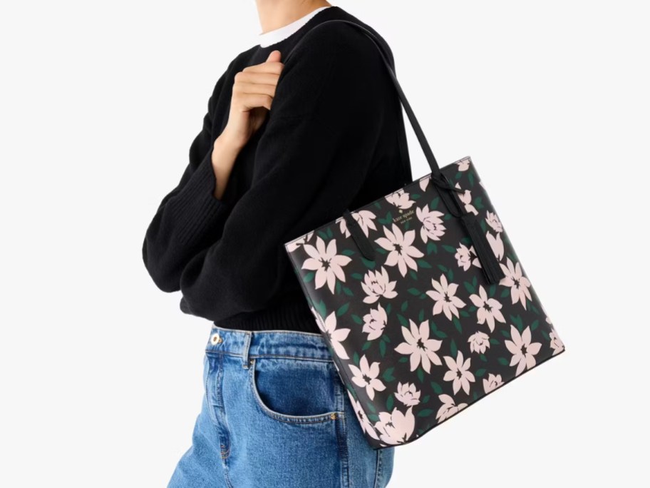 woman wearing a black sweater and jeans with a large black floral print tote bag on her shoulder