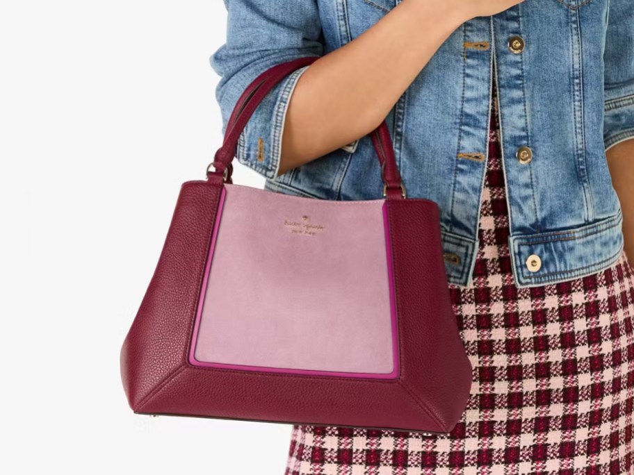 woman wearing a red and white gingham print dress and jean jacket with a dark pink and light pink suede and leather purse on her arm