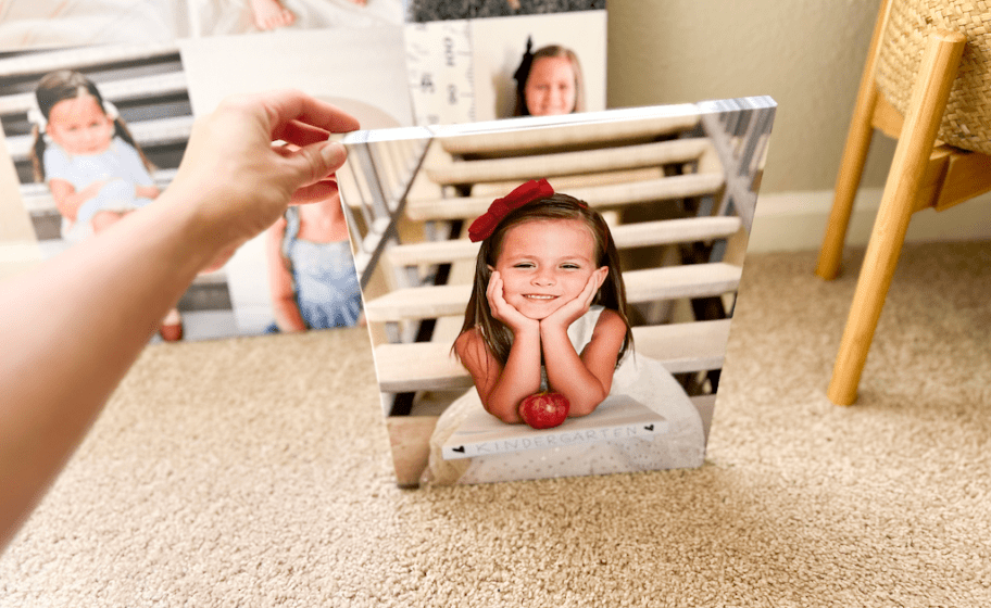 person's arm holding up a canvas photo print of a little girl, more canvas photo prints behind it