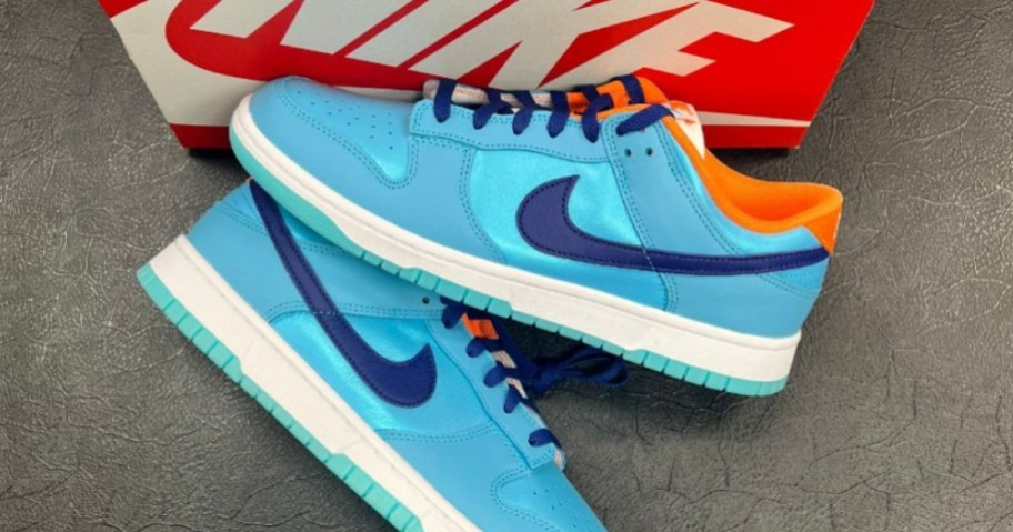 a pair men's Nike Dunks low top shoes in blue, orange Nike box is behind them