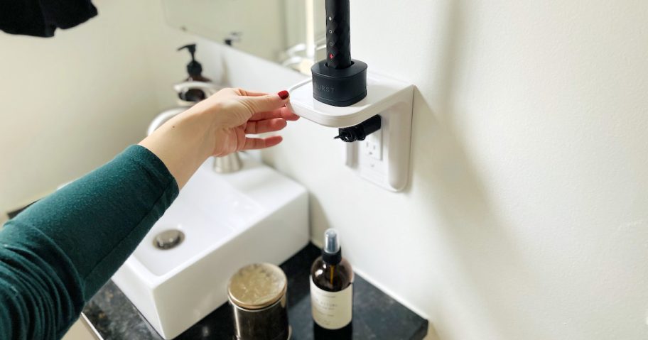 hand holding edge of white outlet shelf with electric toothbrush on top small bathroom storage ideas