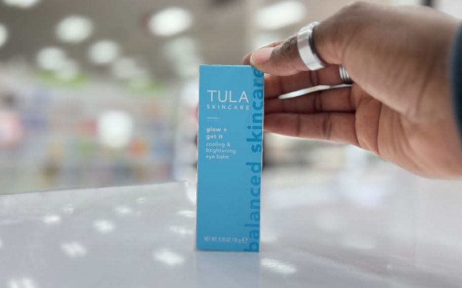 a womans hand reaching for a tula eye balm box on a store counter