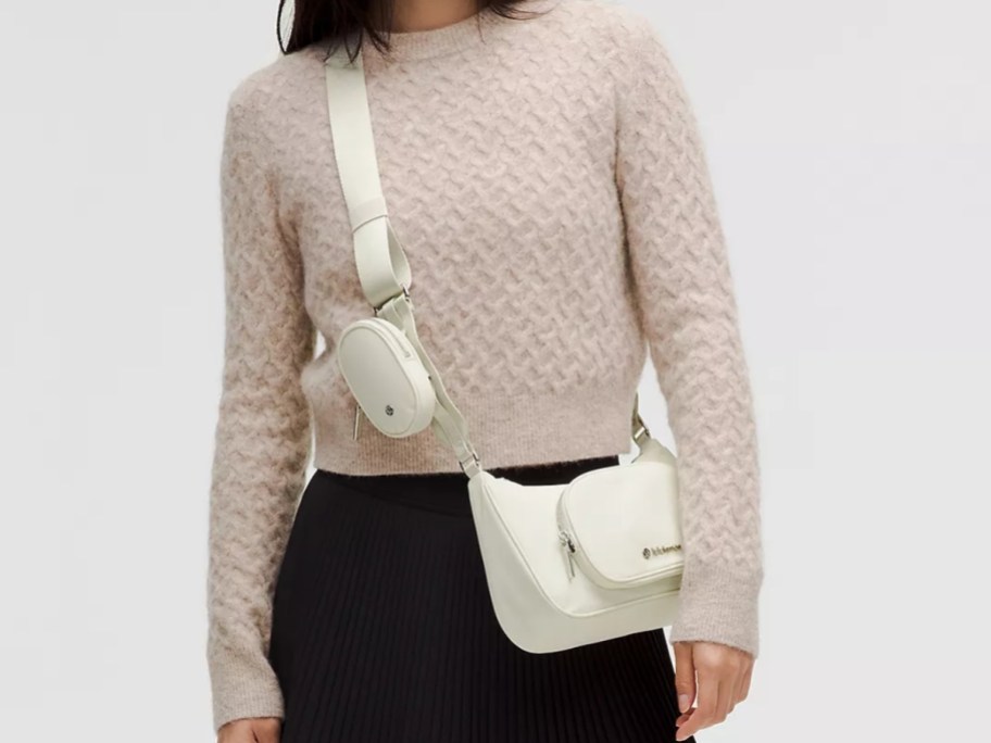 woman in a light tan sweater and brown pants wearing a cream color crossbody bag