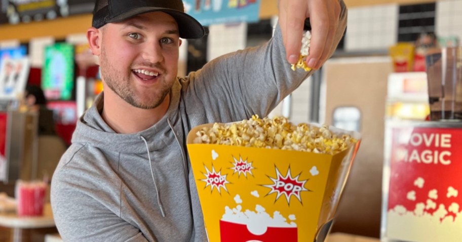 Man holding up bucket of popcorn inside of movie theater