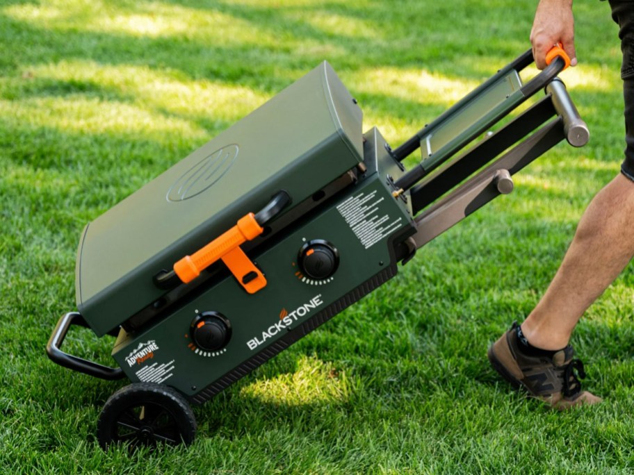 person pulling green folded blackstone grill on grass 