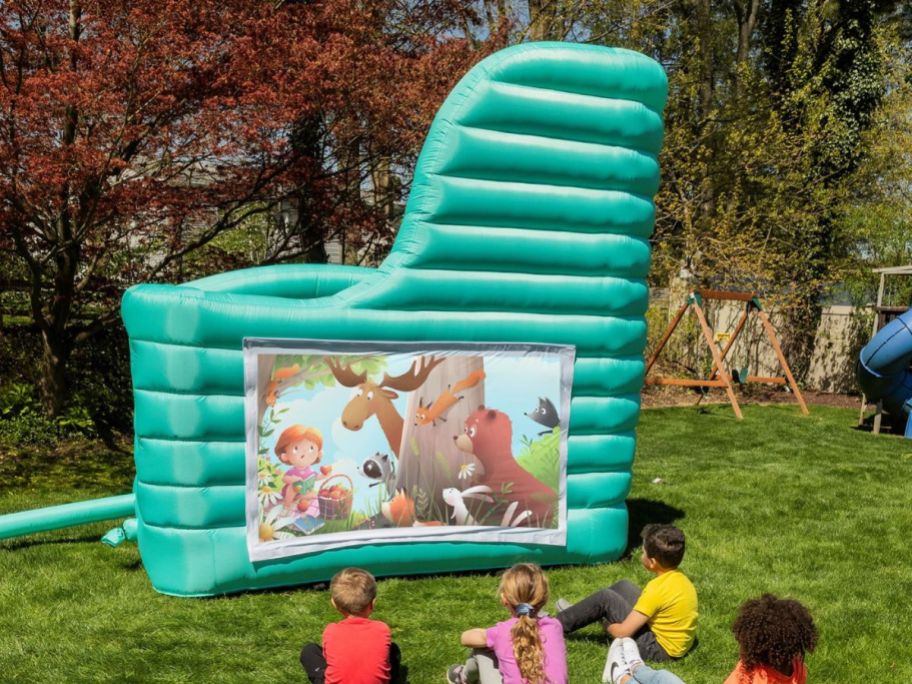 Kids on a lawn watching a giant projector screen on a bounce house