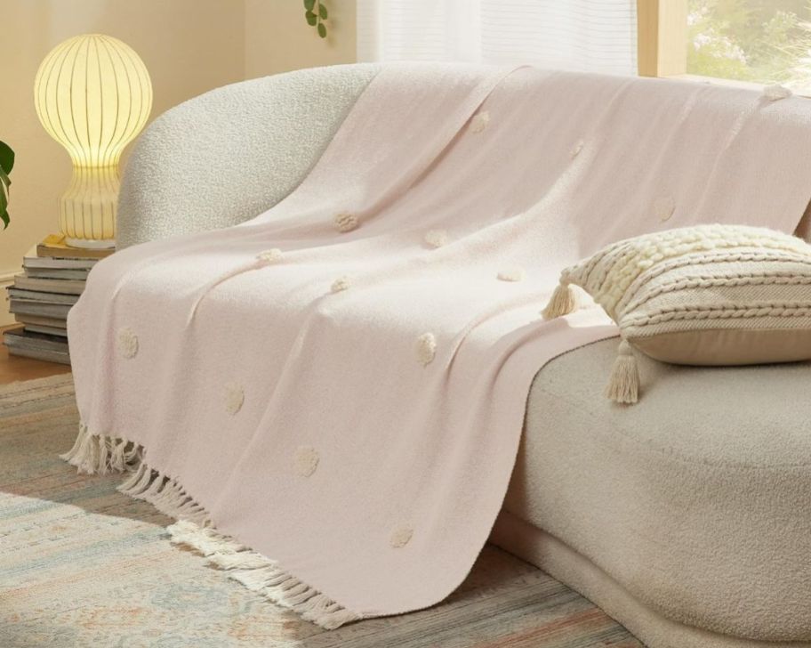 a pink tassel blanket draped over a curved sofa