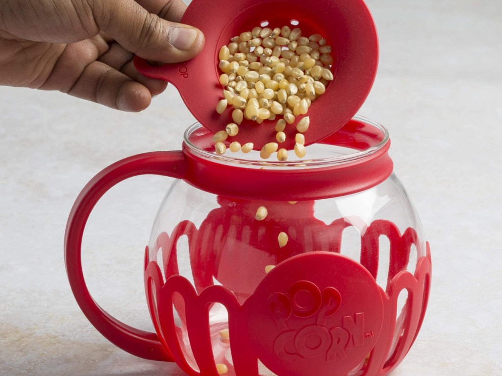 hand pouring popcorn seeds into a glass popcorn popper