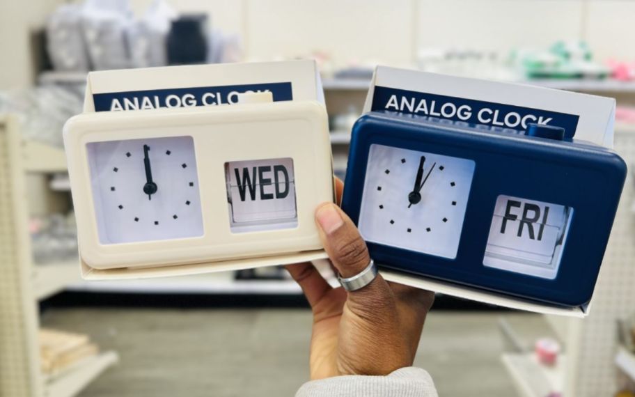 womans hand holding two analog alarm clocks