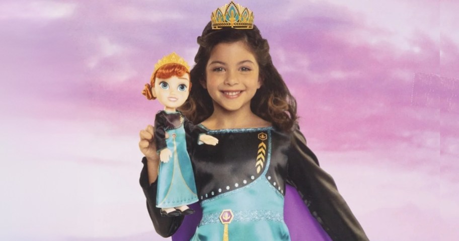 little girl holding a Disney Princess Anna doll and the girl is wearing a matching Anna dress and crown