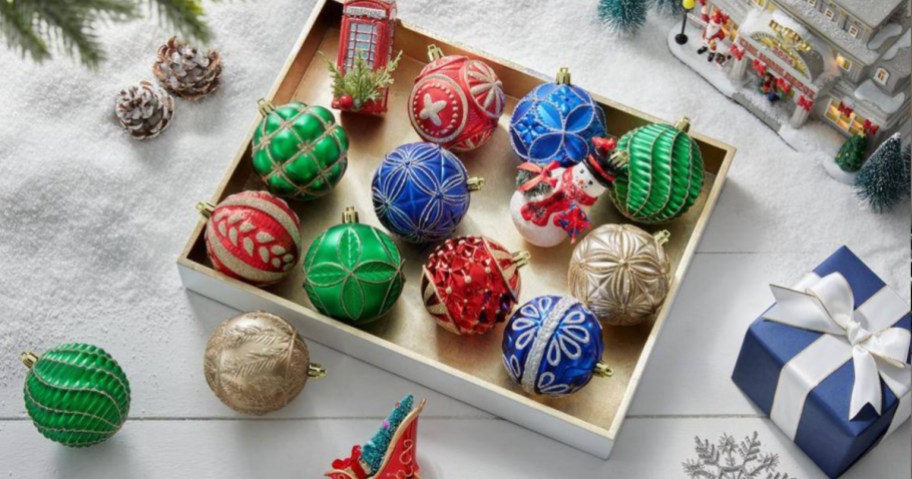 Box of Christmas ornaments on ground next to artificial snow