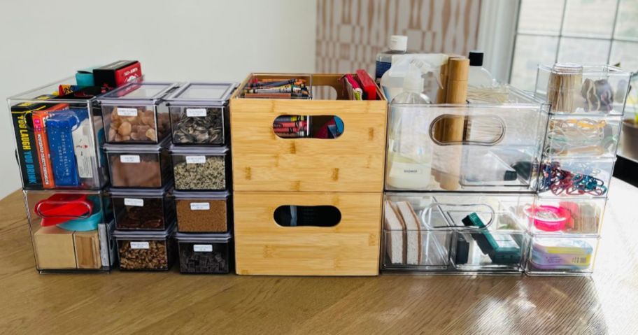 various home organizer bins in clear plastic and light color wood stacked and beside each other on a table