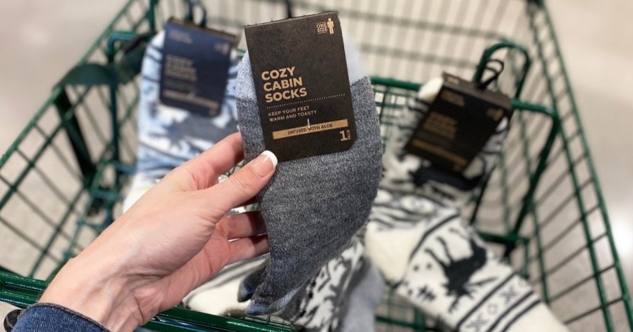 hand holding up a grey pair of cozy socks in front of shopping cart with more