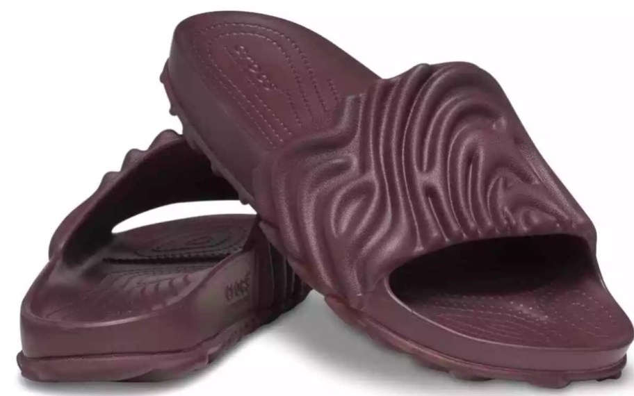 a pair of Crocs slides shoes in a dark purple brown color, the pattern is a wavy style