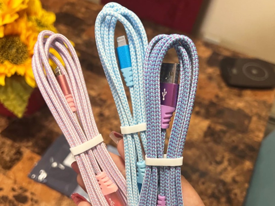 hand holding pink, blue, and purple iphone charging cables