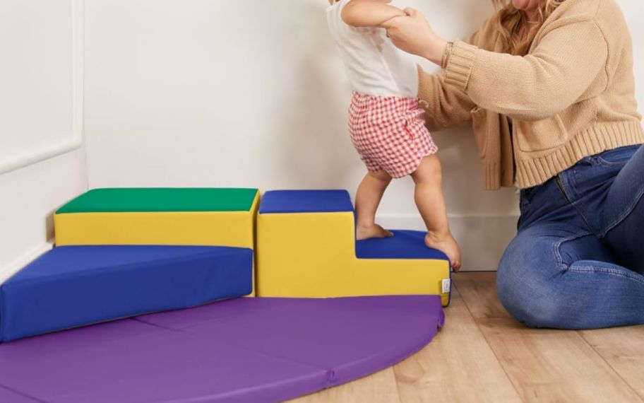 a woman helping a baby decend the steps from the Summit Step corner climber