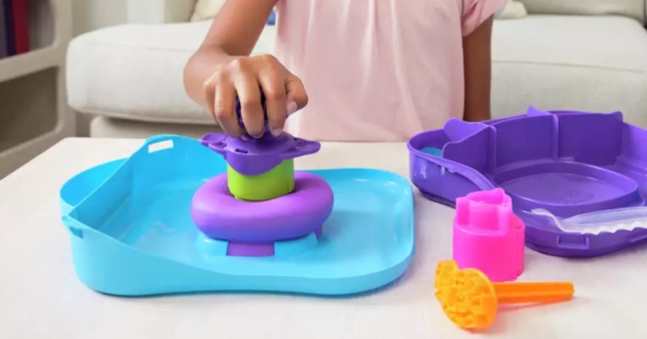 little girl playing with a Kinetic sand playset in a blue base with purple sand and various tools