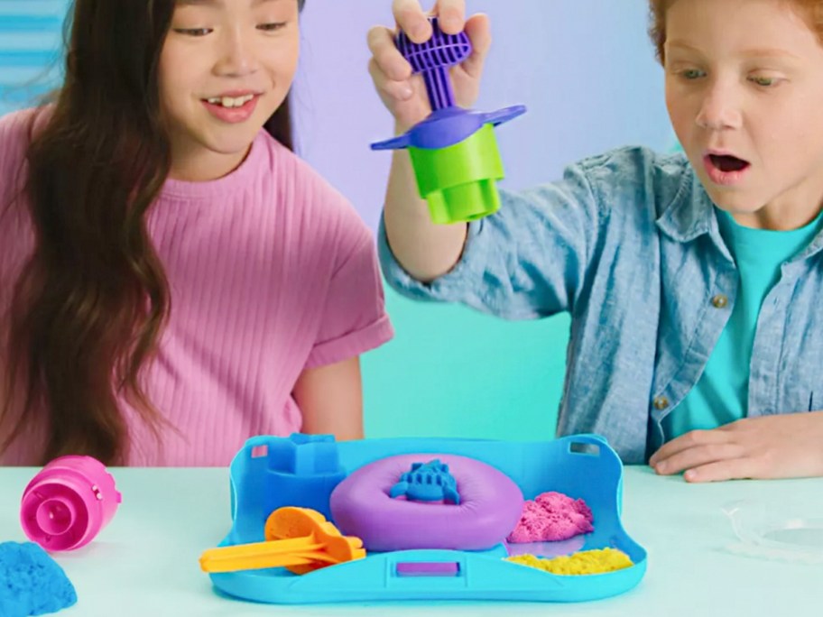 boy and girl playing with kinetic sand toy on table