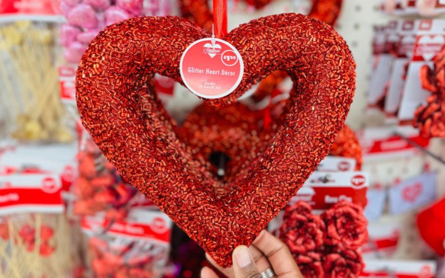 a womans hand grabbing a glitter heart wreath decor from a store display