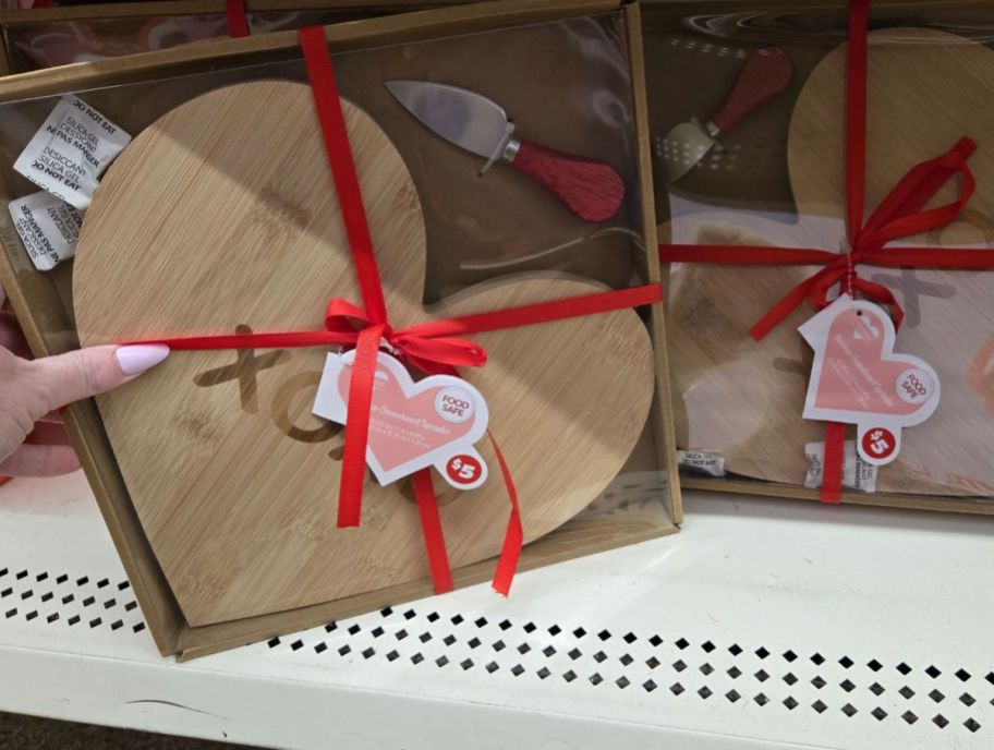 a womans hand grabbing a heart shaped charcuterie board set from a store shelf