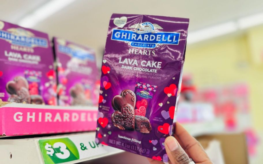 a womans hand grabbing a box chocolate from a store display