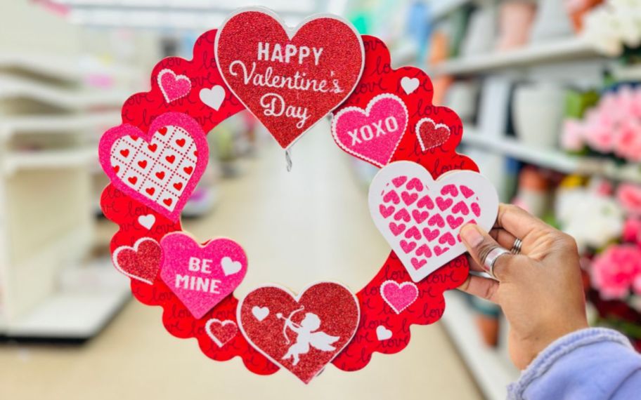 a womans hand holding a wooden valentines wreath wall decor item