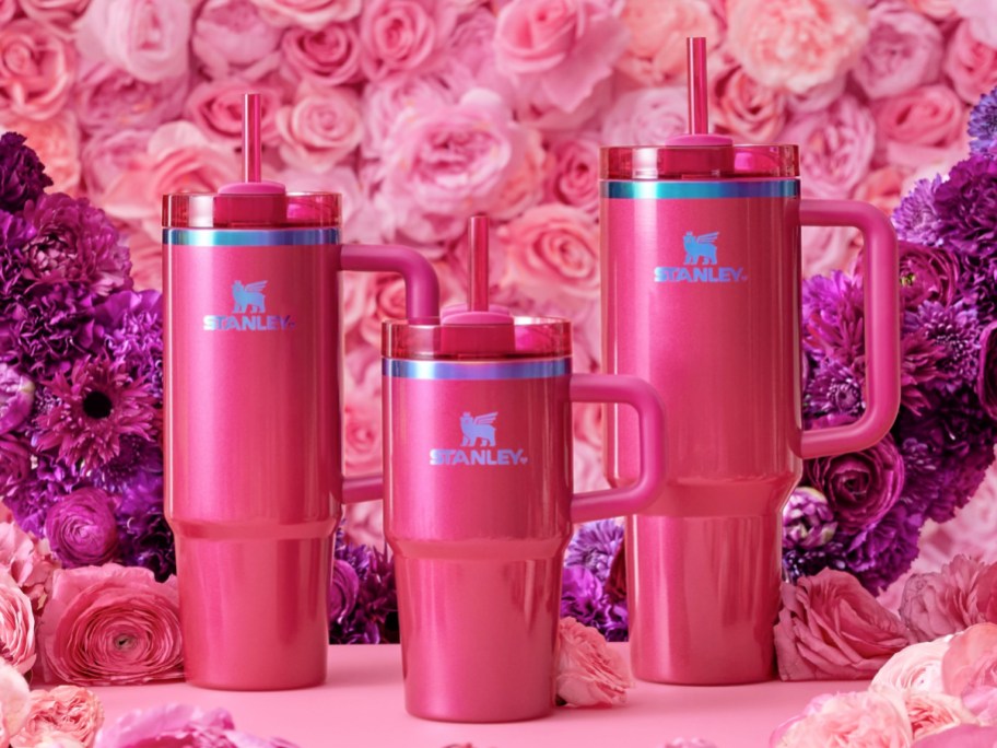 3 hot pink stanley valentines day tumblers in front of pink roses and an assortment of purple flowers