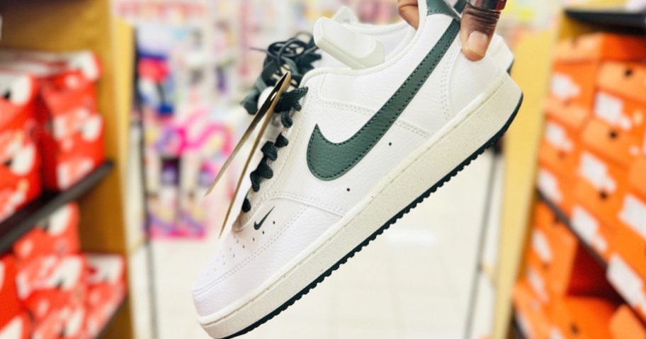 hand holding up a pair of white and green nike sneakers in store