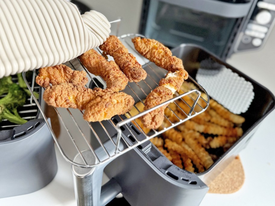 taking tray of chicken strips from basket of fries in air fryer