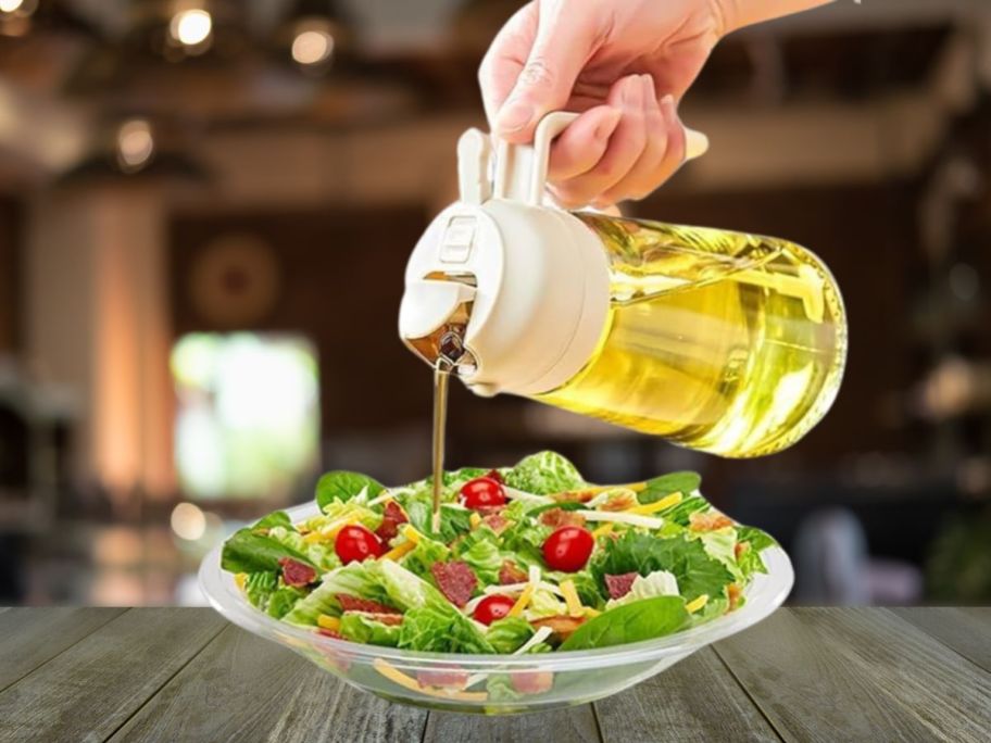 hand using olive oil dispenser to pour oil on salad